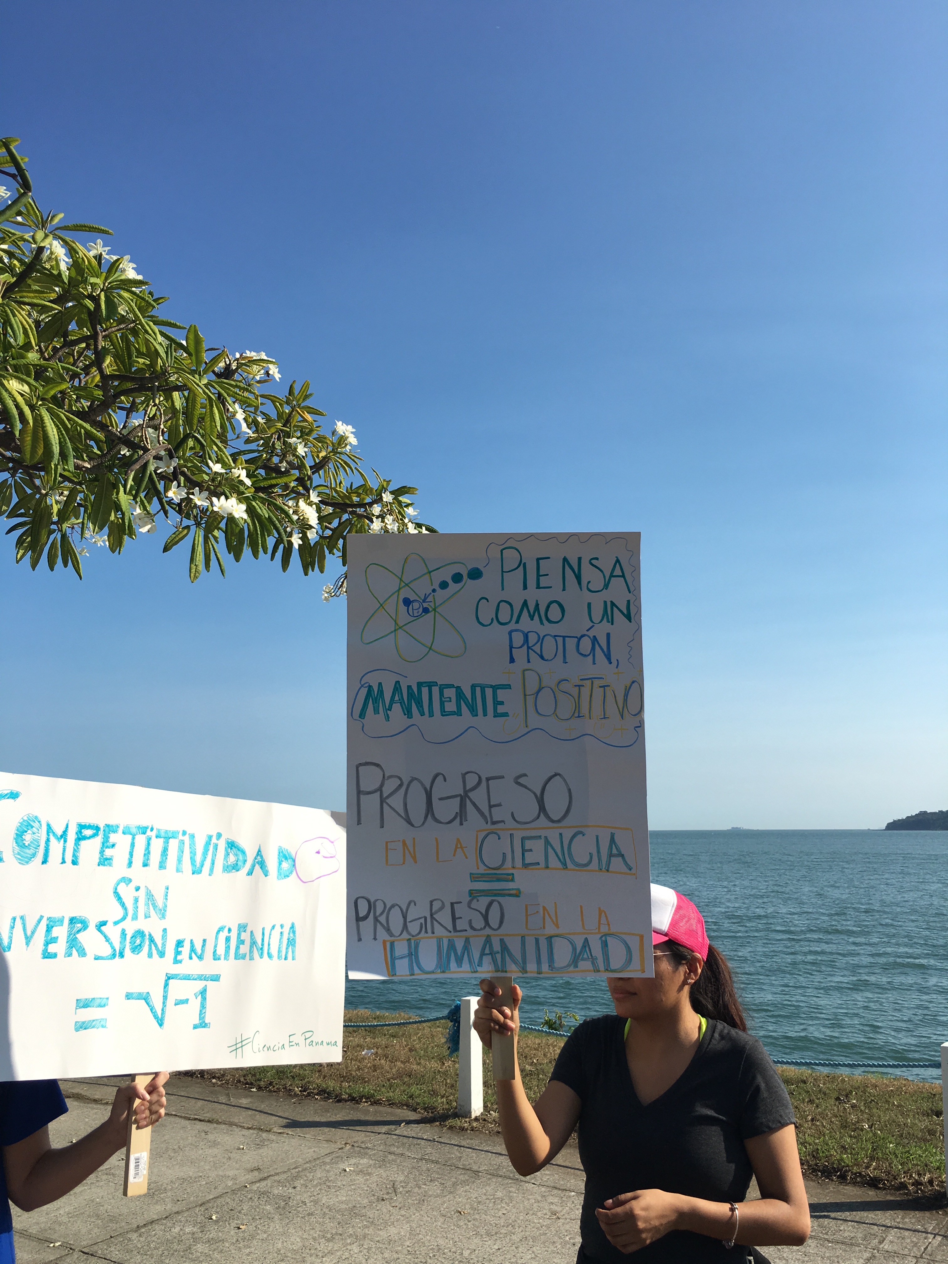 Two posters. The first reads, "A country's competitiveness without investment into science equals the square root of negative one." The second poster reads, "Think like a proton, stay positive" and "Progress in science equals progress for humanity."  